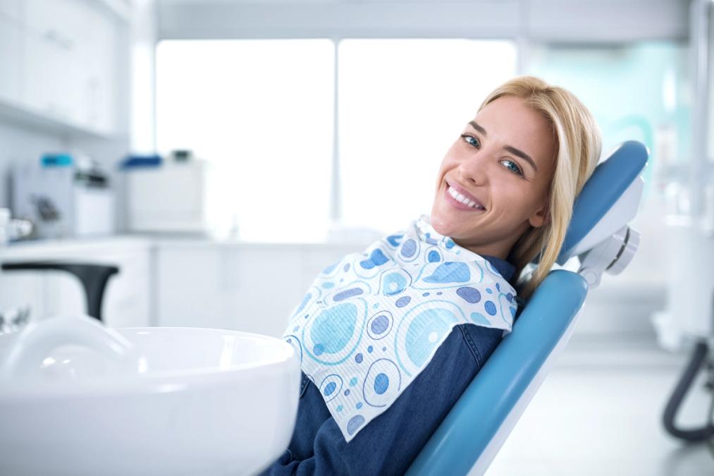 Smiling blonde woman in a dental chair with a patterned bib.