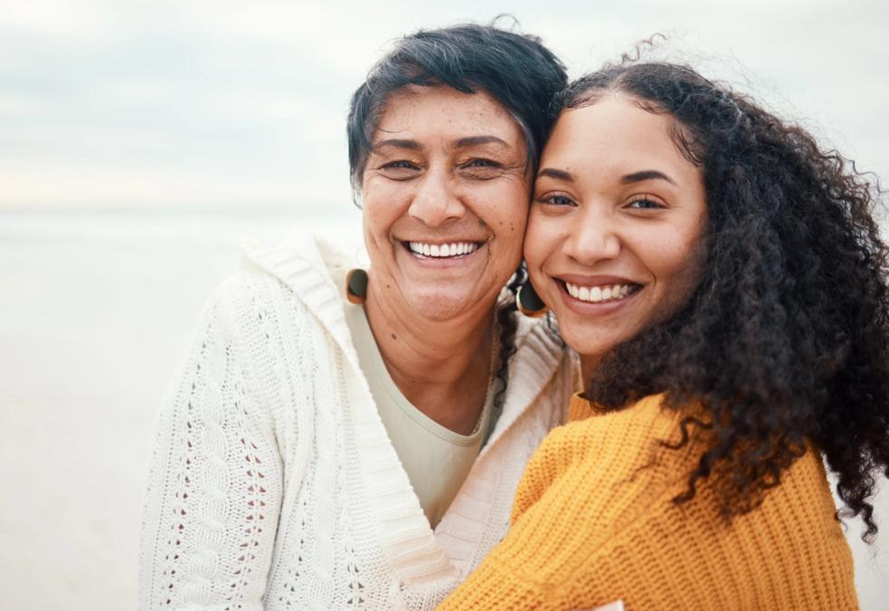Two smiling women, one older and one younger, at a beach.