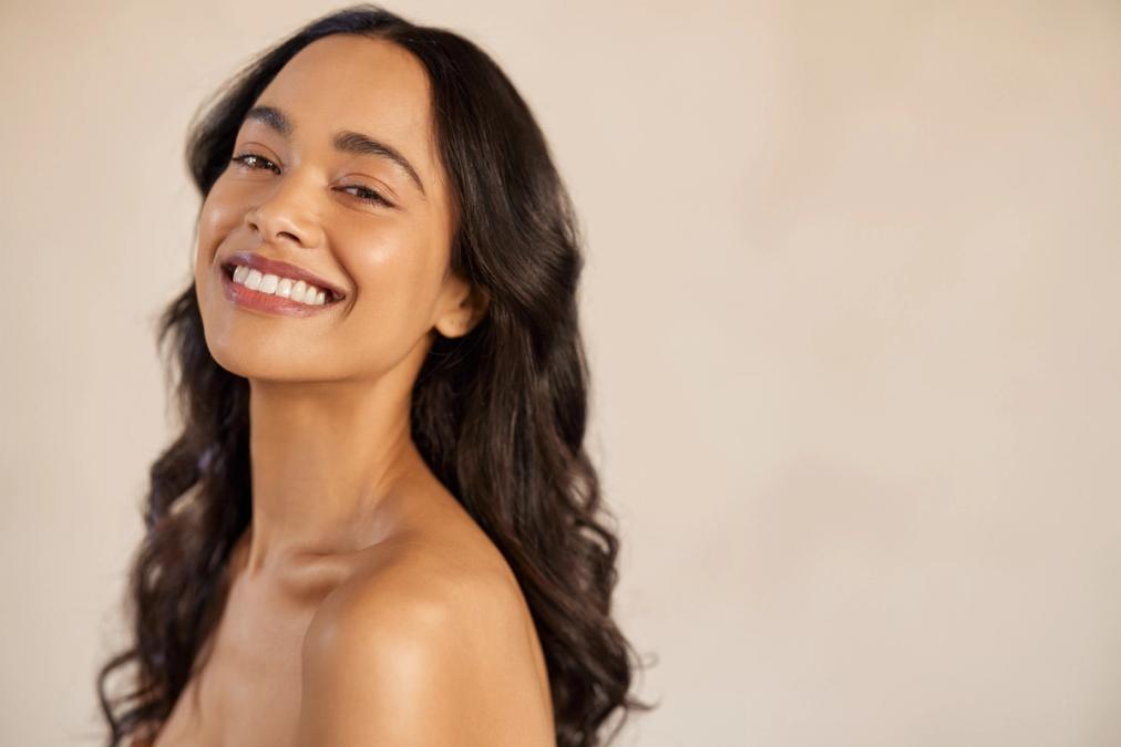 Smiling woman with long dark wavy hair and radiant bare shoulders.