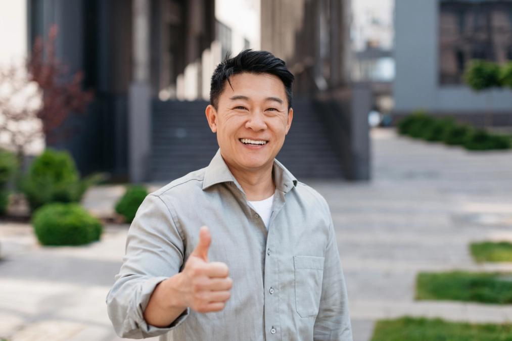 A smiling man in a light shirt gives a thumbs up.