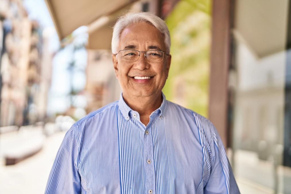 Smiling older man with white hair and glasses in a blue striped shirt.