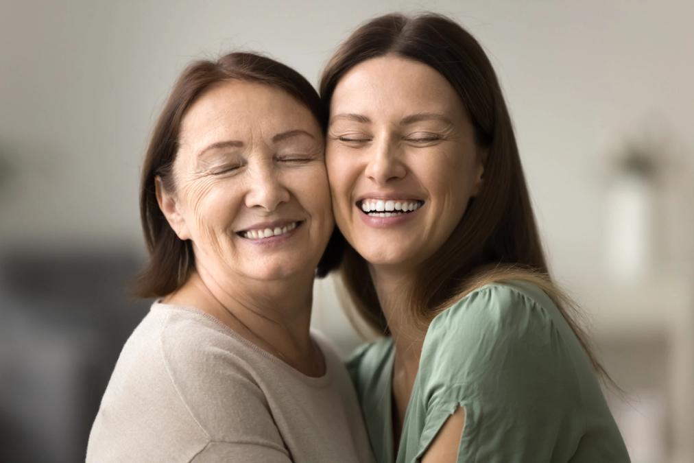 Mother and daughter embracing and laughing with eyes closed.