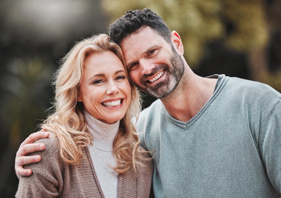 A smiling man and woman, with the man's arm around her shoulder, looking at the camera.