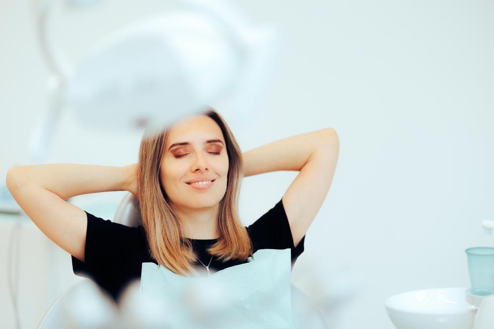 Woman relaxing in a dental chair with eyes closed and hands behind her head.