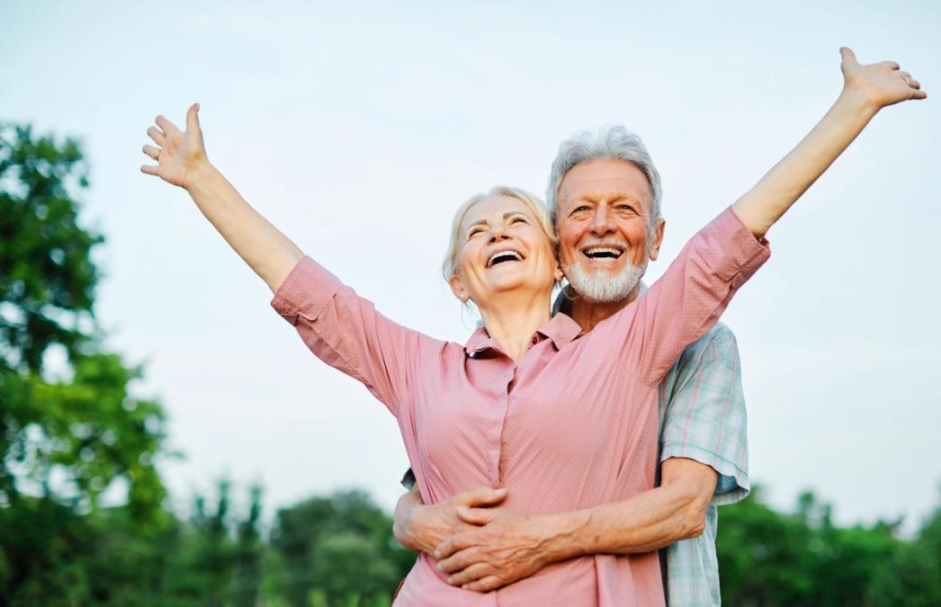 Happy elderly couple embracing with the woman raising her arms in joy.