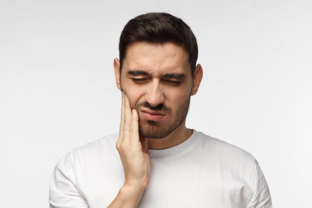 Man grimacing and holding his jaw in pain.