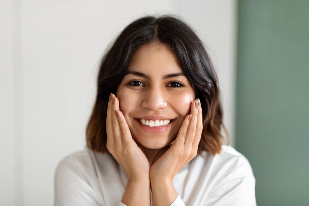 A smiling woman with dark hair holding her hands to her cheeks.